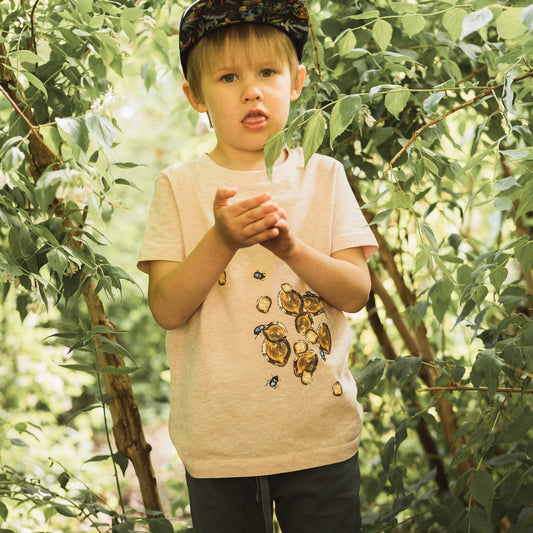 Boy playing in bushes in summertime. wearing a cap, pink t-shirt and green joggers.